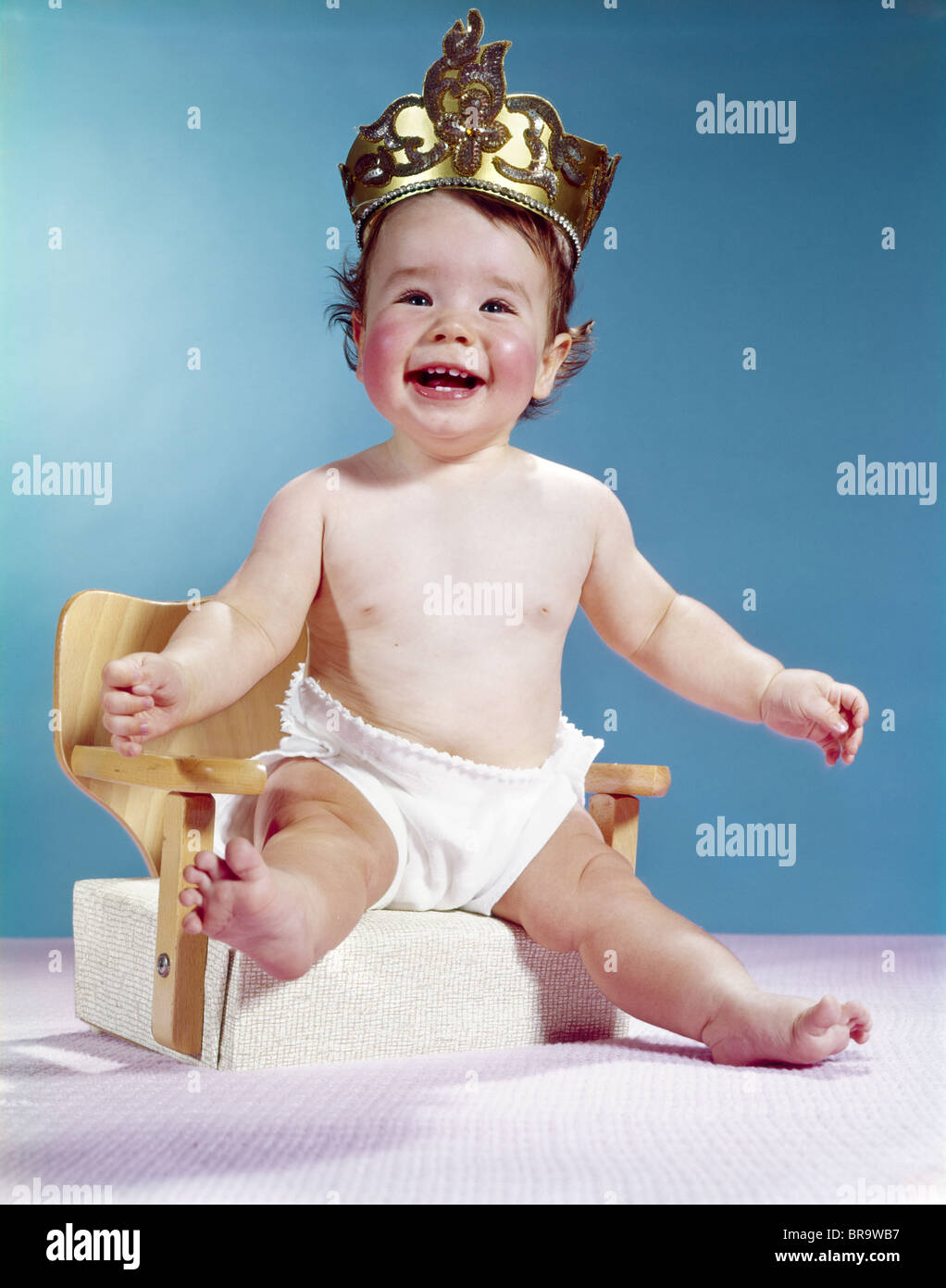 1960ER JAHREN LÄCHELN GLÜCKLICHES BABY TRAGEN KRONE AUF SITZERHÖHUNG STUHL  SITZEND Stockfotografie - Alamy