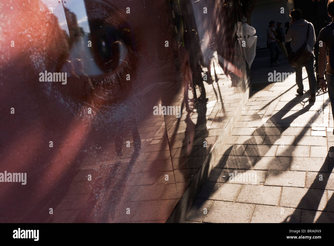 Ein riesiges Auge aus einem Bau Website Horten Uhren Fußgänger und ihre langen Schatten auf Neal Street, London. Stockfoto