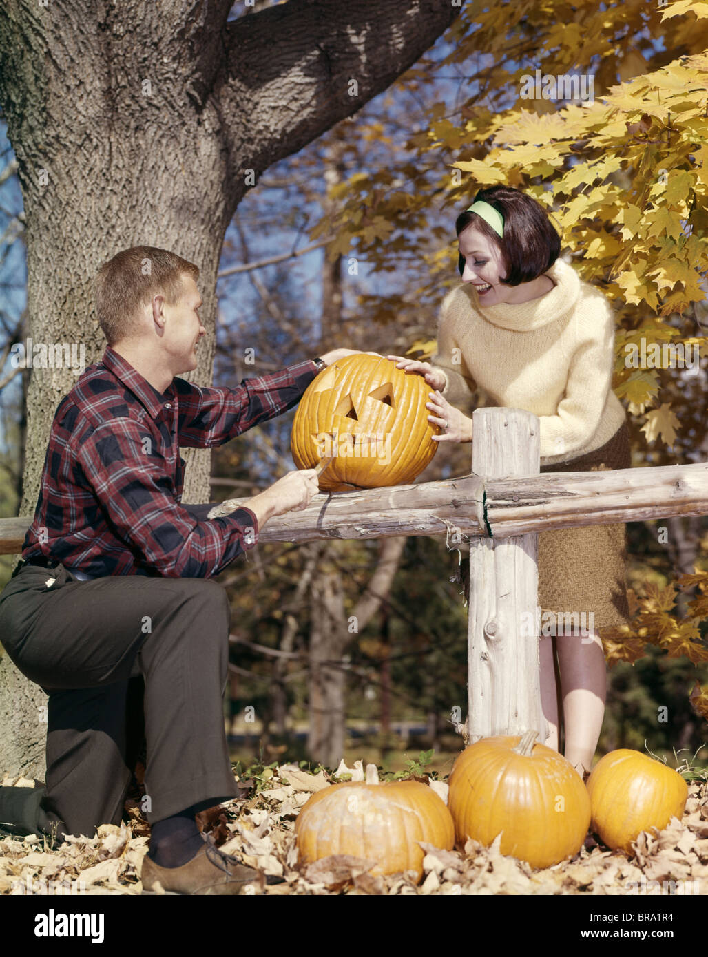 1960ER JAHRE JUNGES PAAR MANN FRAU IM HERBST HOLZ SCHNITZEN HALLOWEEN JACK-O-LANTERN KÜRBIS Stockfoto