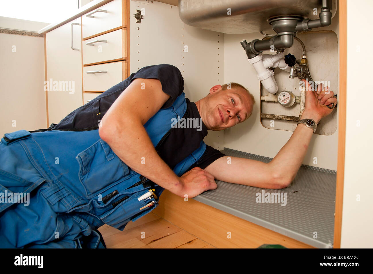 Heizungs- und Sanitär-Techniker reparieren die undichten Rohren unter der Küchenspüle Stockfoto