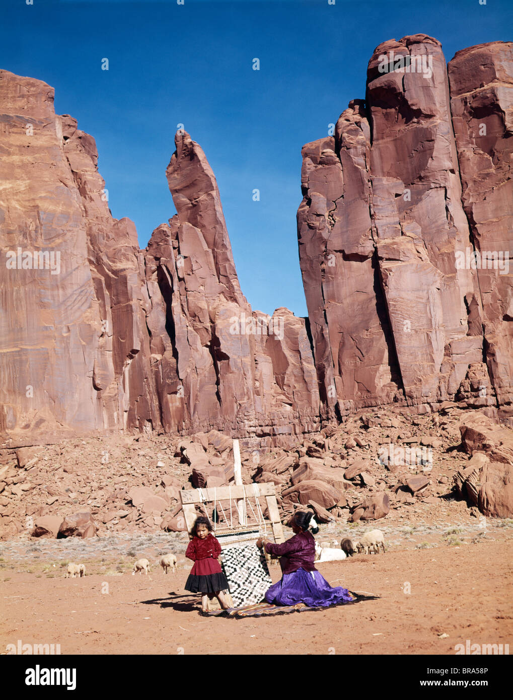1960ER JAHREN NAVAJO MUTTER & TOCHTER AM WEBSTUHL WEBEN HINTERGRUND DER ROTEN FELSEN KLIPPEN VON INDIANER-RESERVAT Stockfoto