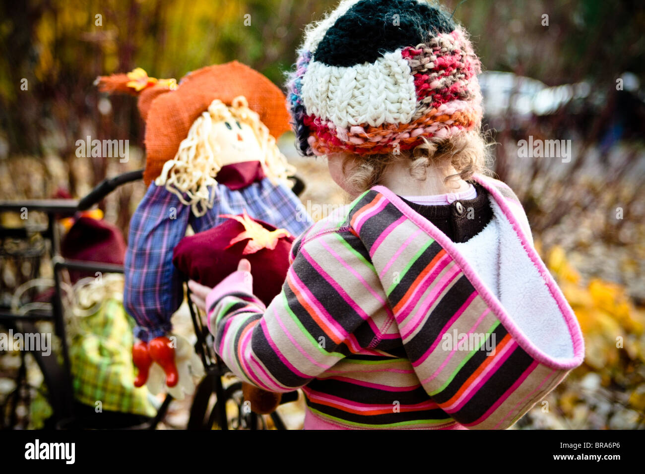 Ein junges Mädchen spielt mit einer Vogelscheuche Ernte Dekoration inmitten der Blätter fallen. Stockfoto