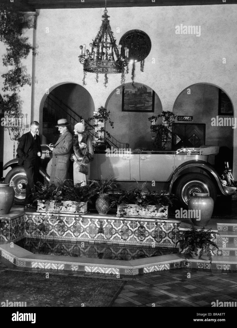 1920ER JAHREN PAAR MANN FRAU MIT VERKÄUFER IN GEHOBENEN AUTO SHOWROOM KAUFEN AUTO Stockfoto