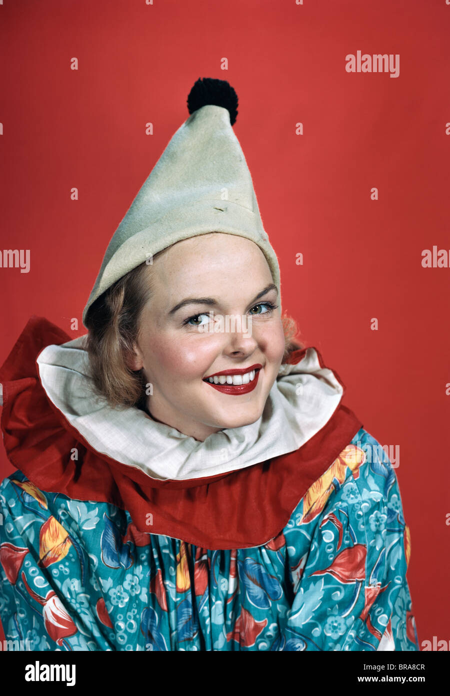 1940S 1950S PORTRÄT LÄCHELNDE FRAU TRAGEN CLOWN OUTFIT ZIPFELMÜTZE POM POM GEKRÄUSELTEN KRAGEN Stockfoto