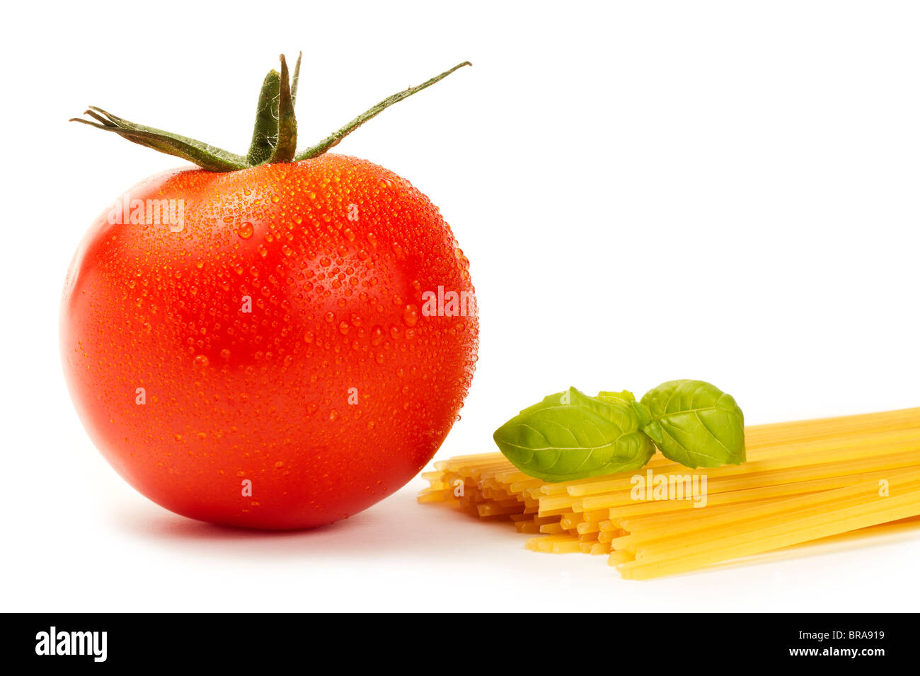 Rohe Spaghetti mit nassen Tomaten und Basilikum auf weißem Hintergrund Stockfoto