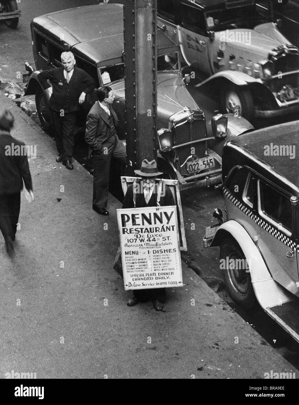 1930ER JAHREN NEW YORK STREET WÄHREND DER DEPRESSION MIT MANN TRAGEN SANDWICH WERBUNG PENNY BORDRESTAURANT Stockfoto