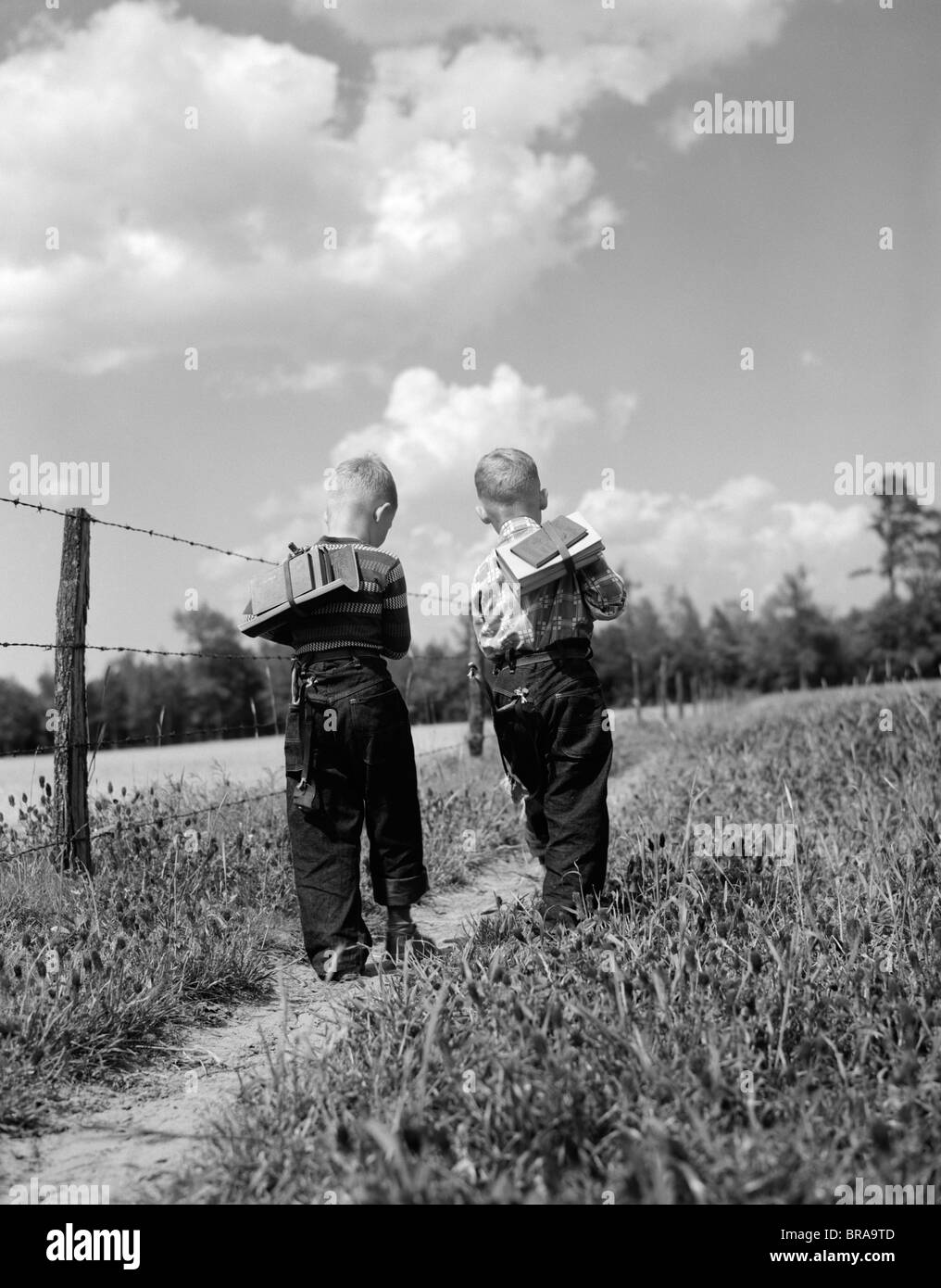 1950ER JAHRE ZURÜCK ANSICHT 2 JUNGS MIT BUCH-PACKS ZU FUß ZUR SCHULE Stockfoto