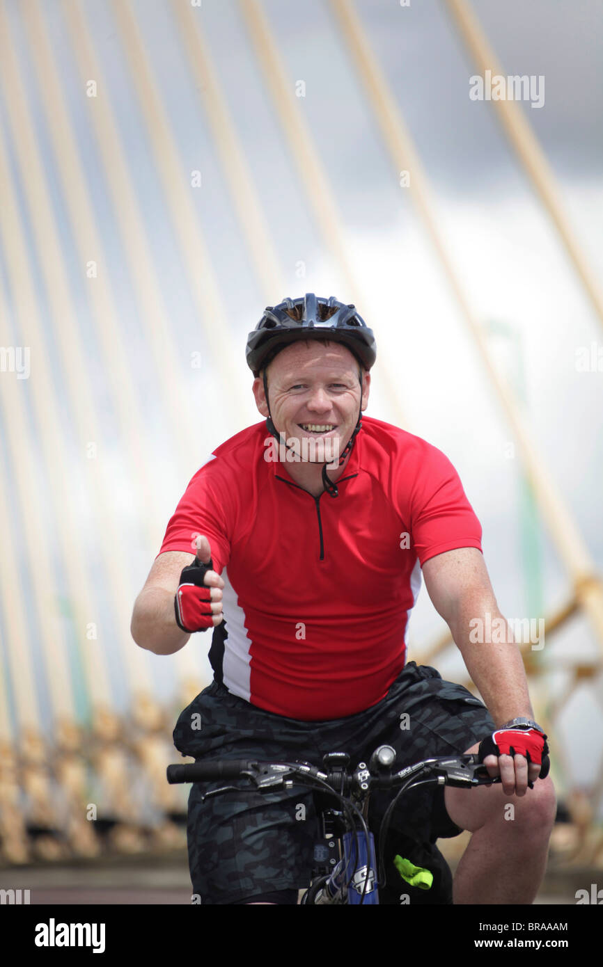 Ein glücklicher Mensch, Radfahren über eine Brücke, die die Daumen aufgeben. Stockfoto