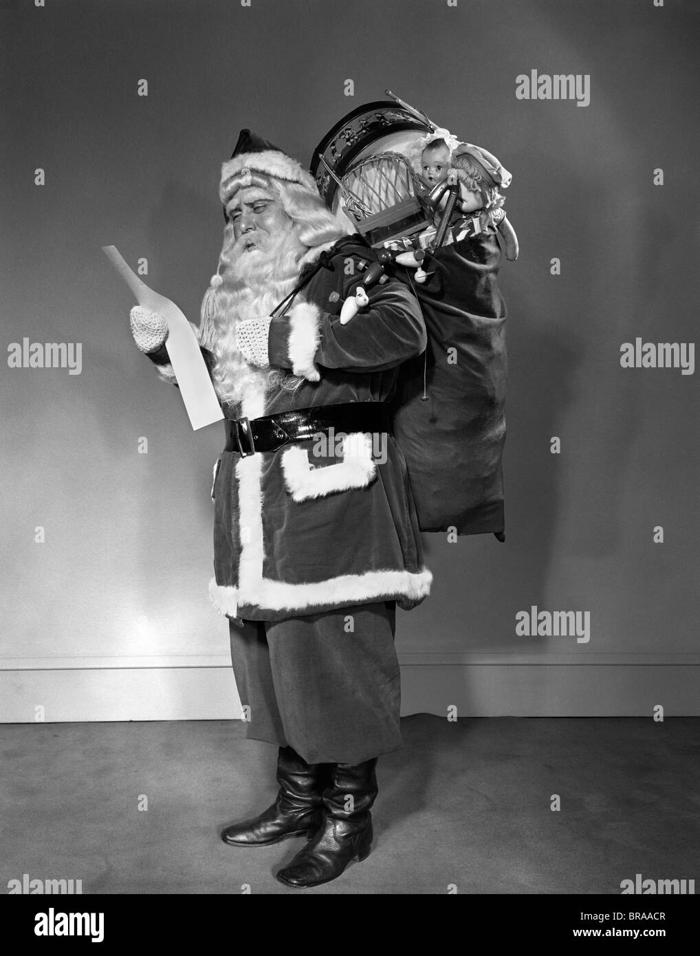 1940ER JAHRE WEIHNACHTSMANN TRAGEN BEUTEL VOLLER SPIELSACHEN LESELISTE Stockfoto