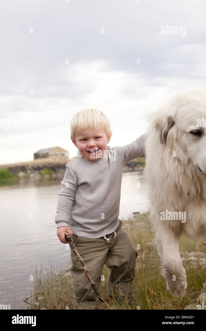 Kleiner Junge hält einen Stock, einen Hund streicheln Stockfoto