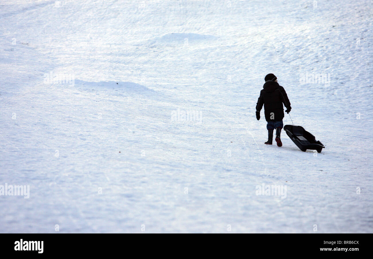 Ein Junge, einen Schlitten bergauf im Schnee ziehen. Stockfoto