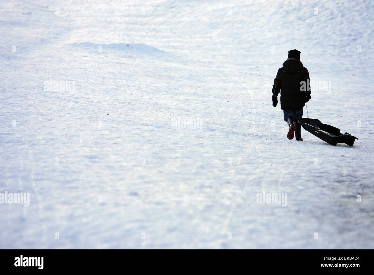 Ein Junge, einen Schlitten bergauf im Schnee ziehen. Stockfoto