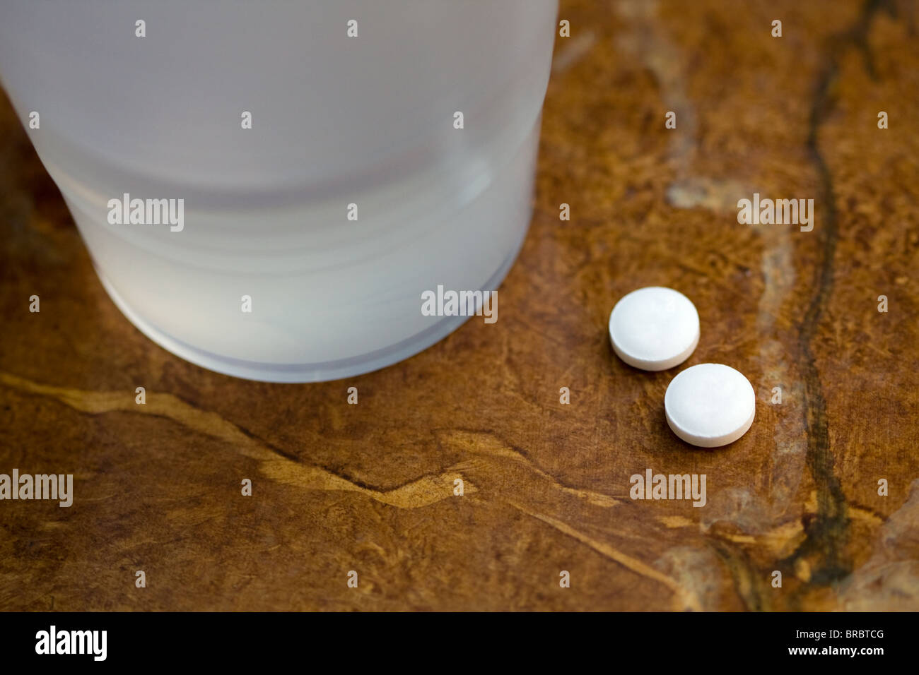 Zwei Aspirin auf einem Tisch mit einer Tasse Wasser Stockfoto