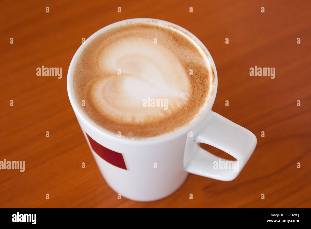 Tasse Tasse Cafe Latte Kaffee in Form eines Herzens in den Schaum auf einem braunen Holz- Tabelle von oben. England, Großbritannien, Großbritannien. Stockfoto