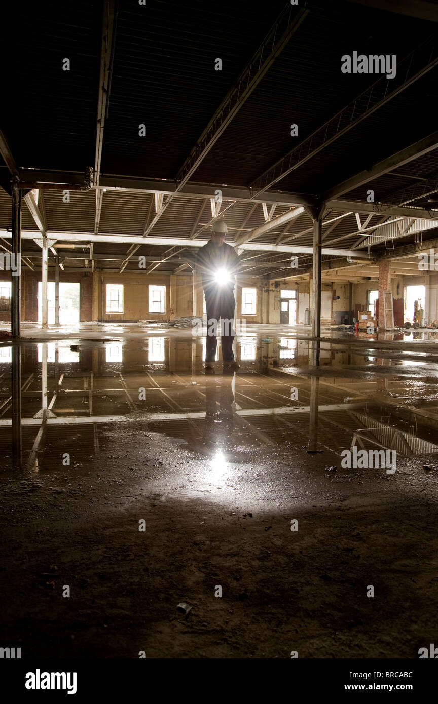 Abriss-Worker Holding Taschenlampe im alten industriellen Gebäude mit Wasserpfütze im Stock, Philadelphia, USA Stockfoto
