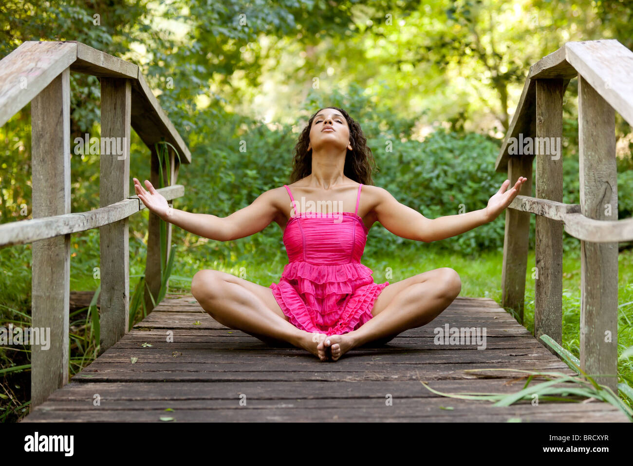 sportliche Frau in rosa Kleid praktizieren Yoga auf hölzerne Brücke im park Stockfoto