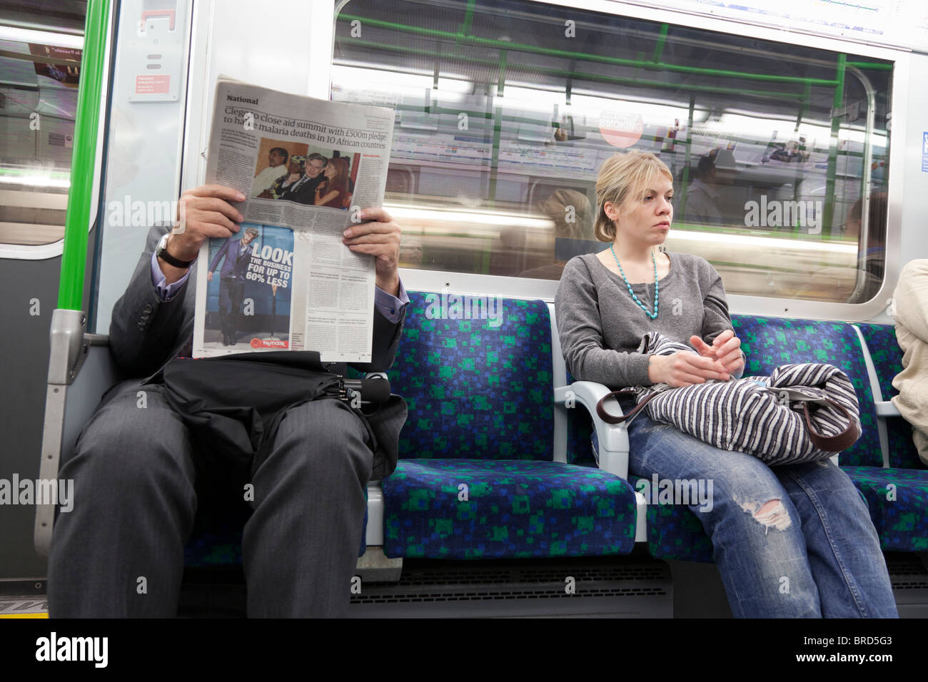 männlichen Passagier Zeitunglesen mit gelangweilt aussehende Frau sitzend auf London Underground Stockfoto