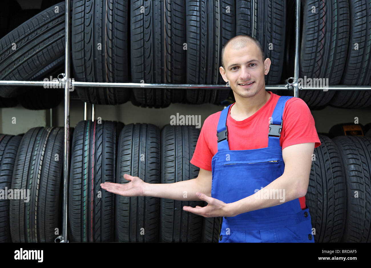 Ein Lächeln auf den Lippen Mechaniker in einer Garage stehen neben einem Rack voller Reifen und eine positive Geste Stockfoto