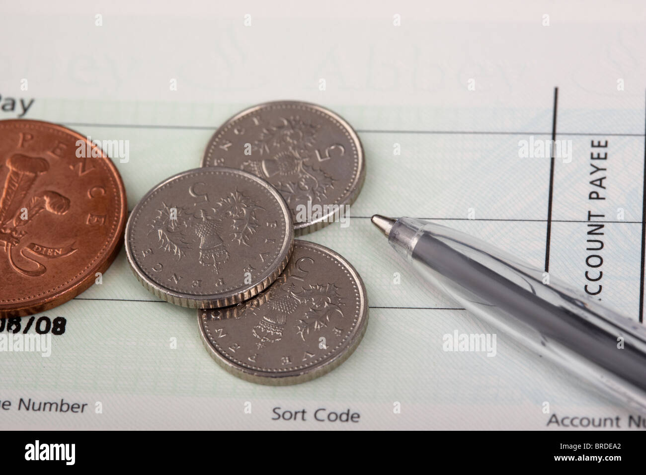 Münzen auf ein Scheckheft mit Stift Stockfoto