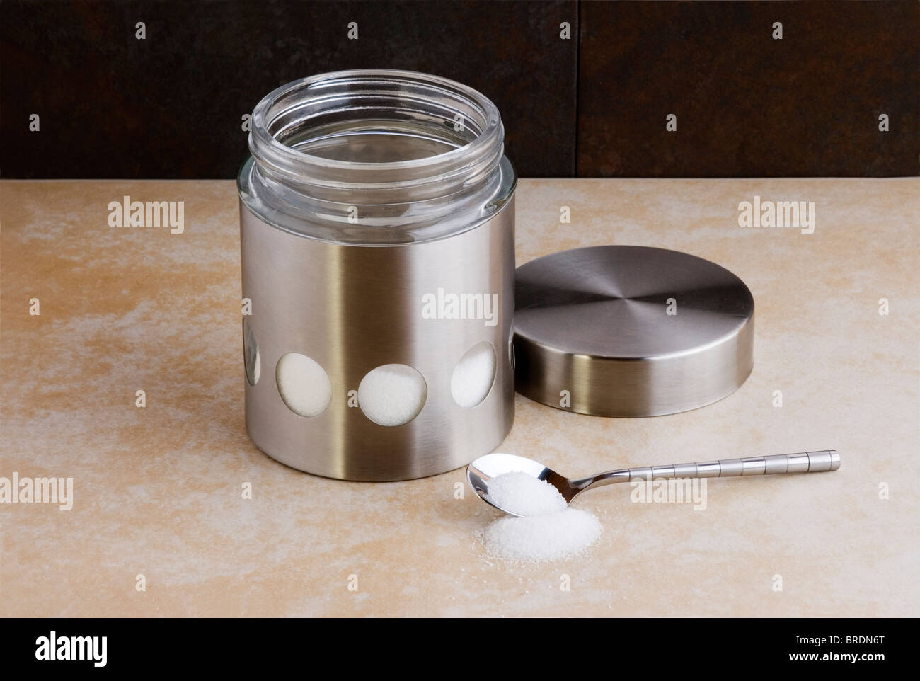 Edelstahl und Glas Zucker Behälter, mit einem Teelöffel auf eine Arbeitsplatte. Stockfoto