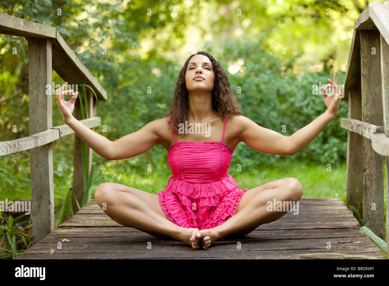junge Frau sitzt auf Holzbrücke im Lotussitz Stockfoto