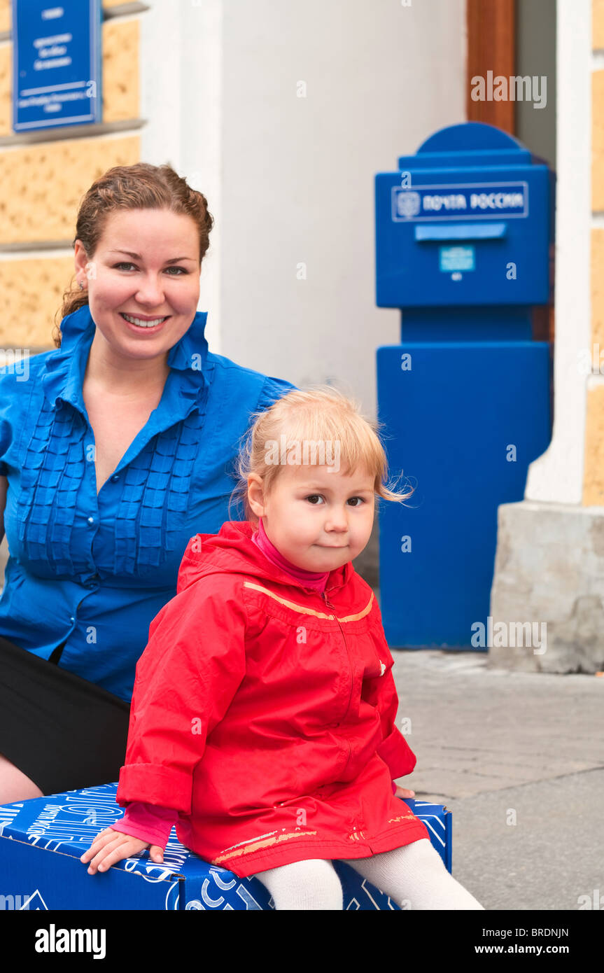 Ein junges Mädchen und kleine Kind sitzt auf einer Kiste in der Nähe von den Verbindungsbüros der russische Post. Postfach Stockfoto