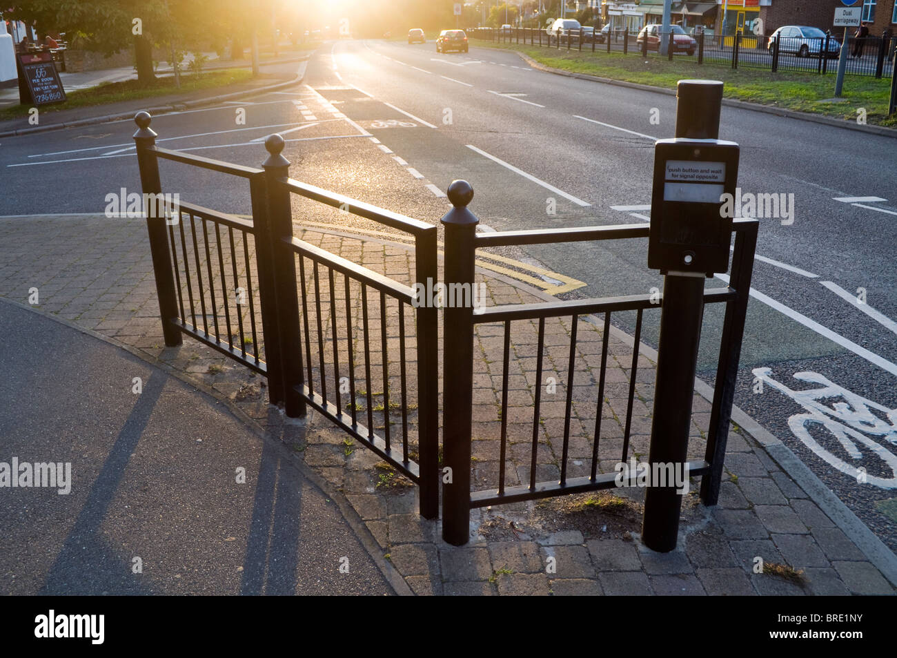 Atmosphärischen Abend tiefstehende Sonne über den Bürgersteig, Geländer und öffentlichen Straßenquerung in Uxbridge Road West London UK Stockfoto