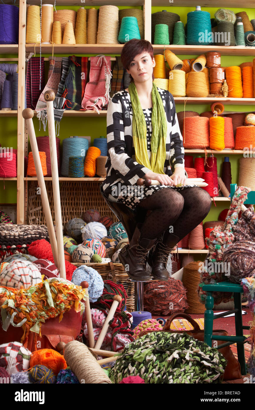 Junge Frau sitzt auf Schemel mit Stricknadeln vor Garn Display Stockfoto