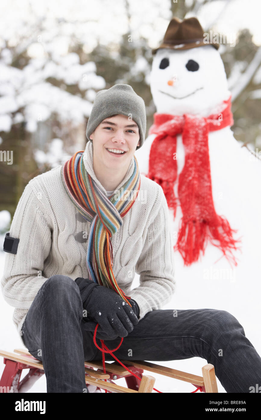 Teenager mit Schlitten neben Schneemann Stockfoto