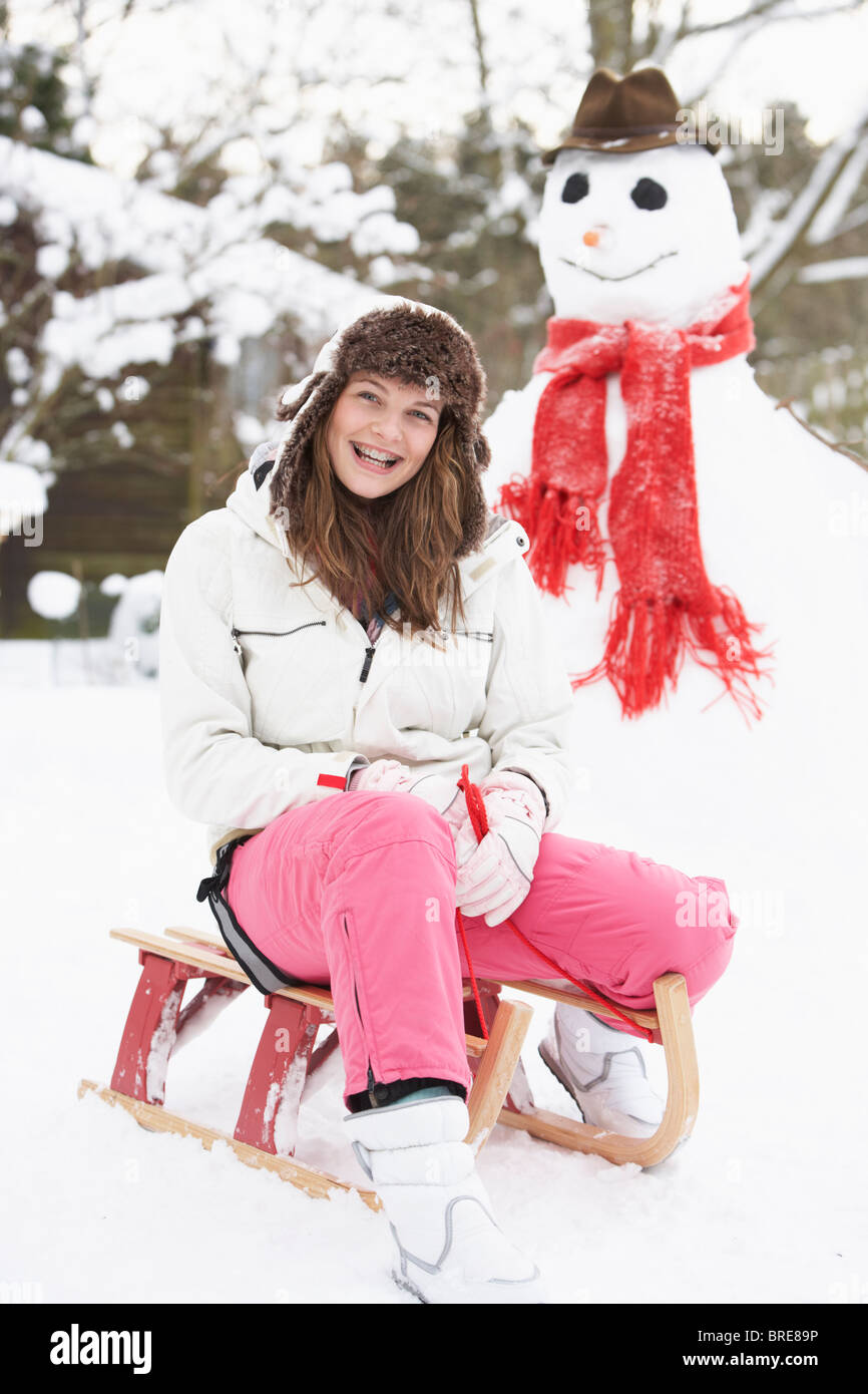 Teenager-Mädchen mit Schlitten neben Schneemann Stockfoto