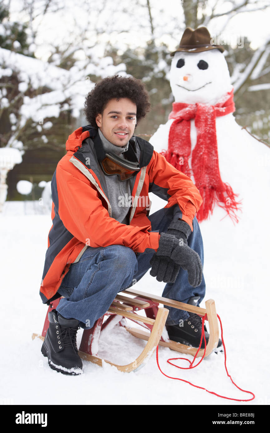 Mann mit Schlitten neben Schneemann Stockfoto