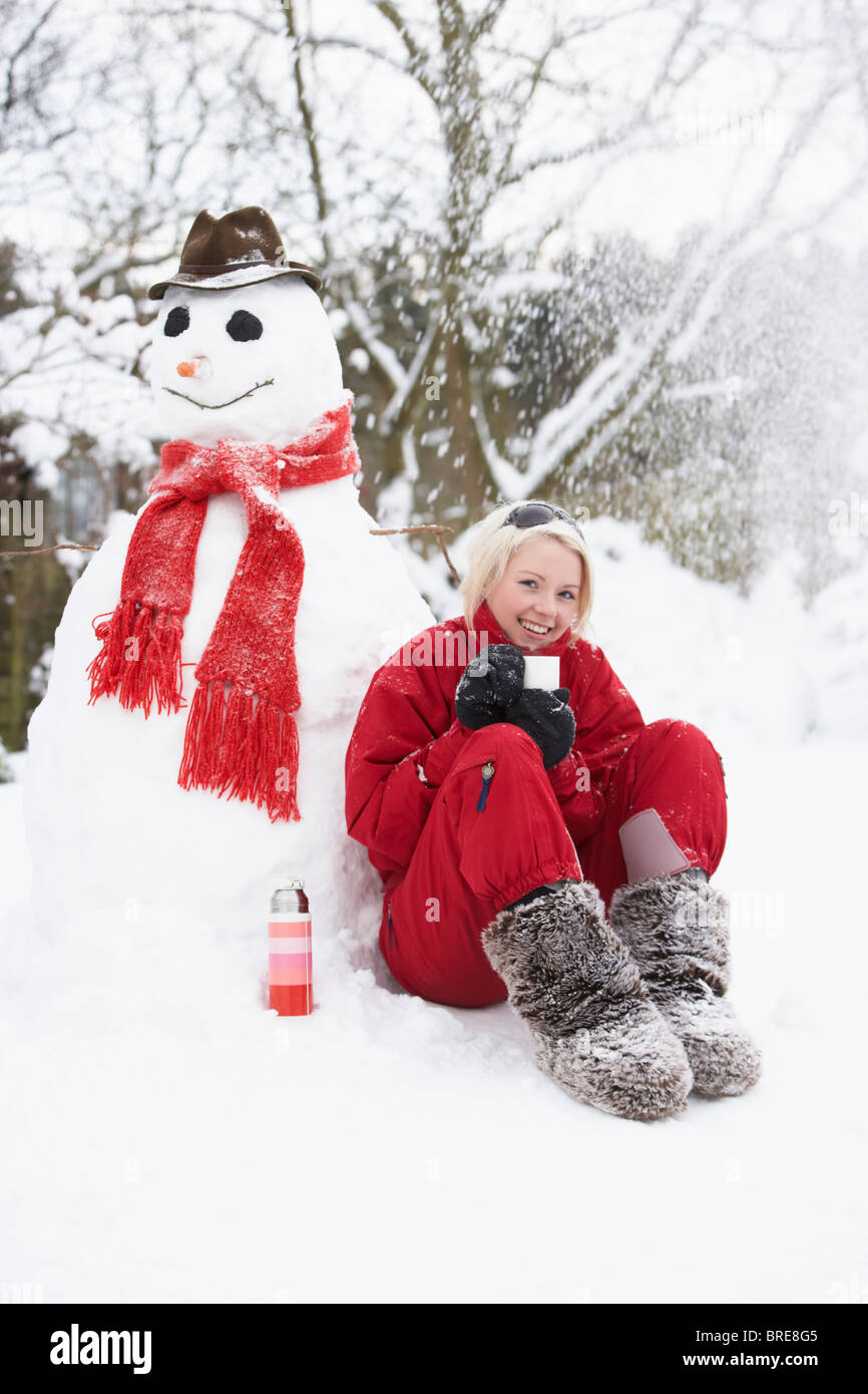 Teenager-Mädchen neben Schneemann mit Kolben und Heißgetränk Stockfoto