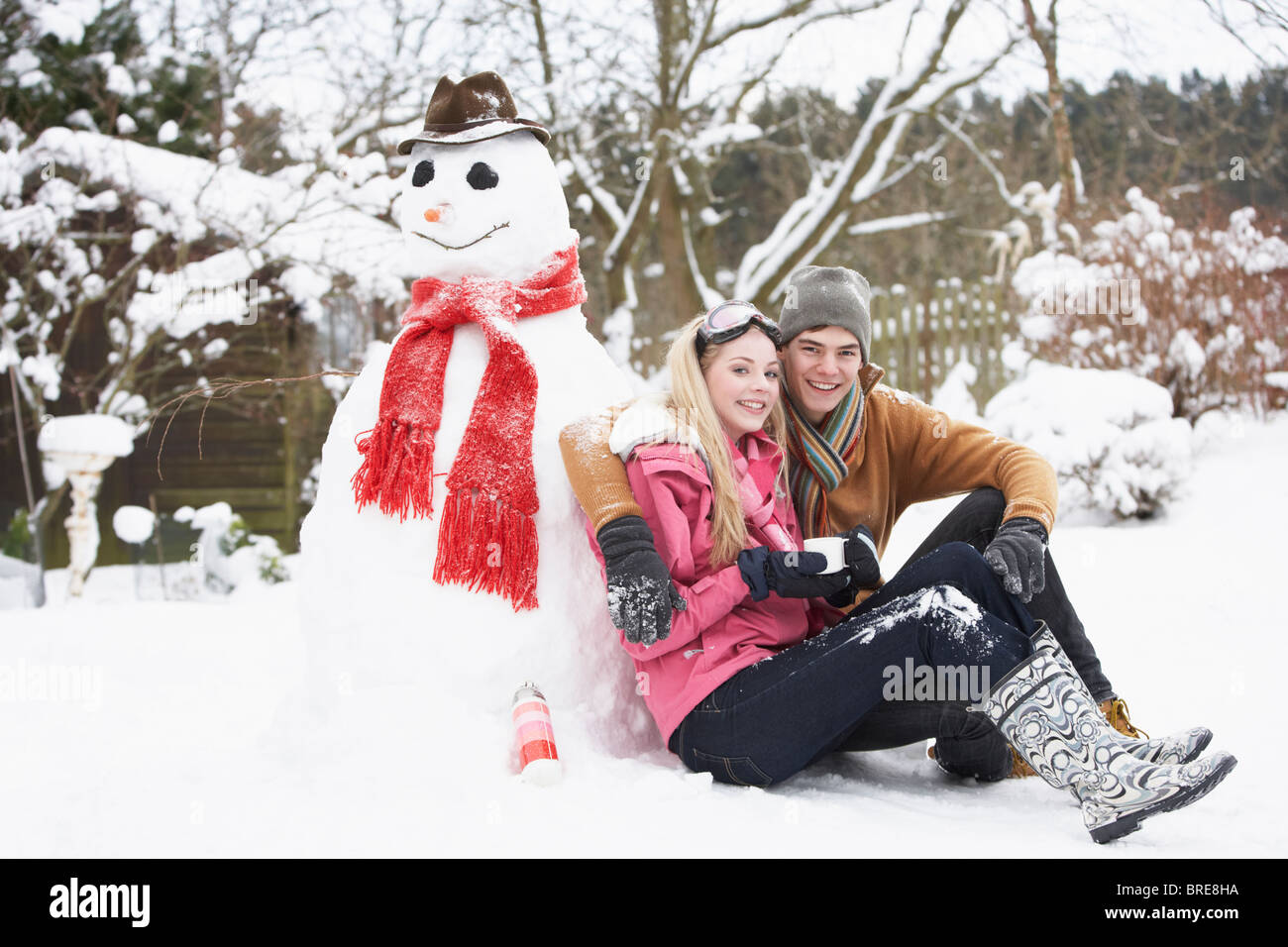 Teenager-paar In Winterlandschaft neben Schneemann mit Kolben und Heißgetränk Stockfoto