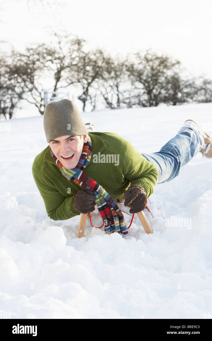Junger Mann reitet auf Schlitten In Schneelandschaft Stockfoto