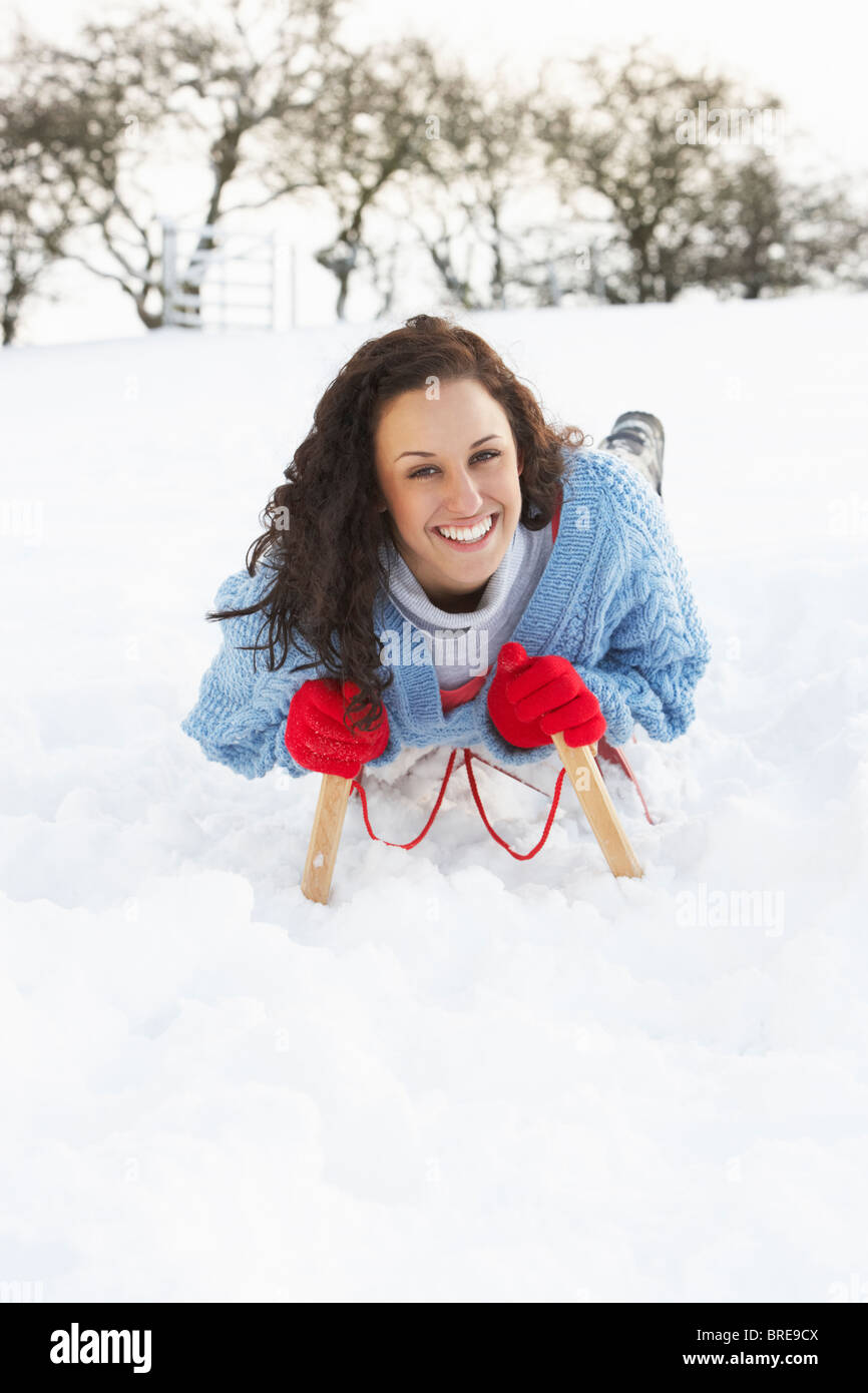 Junge Frau Reiten auf Schlitten In Schneelandschaft Stockfoto