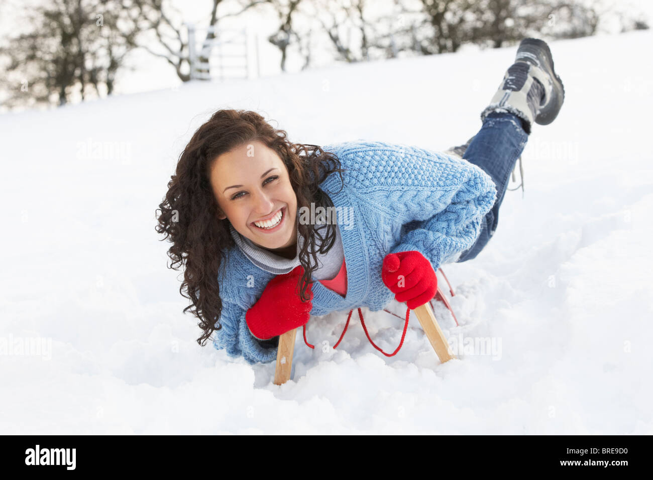 Junge Frau Reiten auf Schlitten In Schneelandschaft Stockfoto