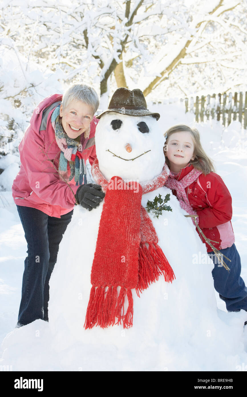 Junges Mädchen mit Großmutter Gebäude Schneemann im Garten Stockfoto