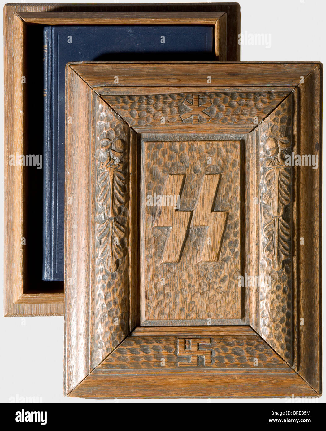 Eine SS-Präsentationskoffer aus Holz für "Mein Kampf"-Eiche mit einem dunkel gefärbten äußeren. Der Deckel (zwei Innenleisten fehlen/werden wiederhergestellt) hat die in der Mitte geschnitzten SS-Runen, die von einem knöcheligen erhöhten Kreis mit Hakenkreuz und Eichenblättern umgeben sind. Abmessungen 25,5 x 19,5 x 8 cm. Im Inneren befindet sich die ungekürzte Ausgabe von 1934 mit der blauen Stoffbindung: Historisch, historisch, 1930er, 20. Jahrhundert, Waffen-SS, bewaffnete SS-Division, bewaffneter Dienst, bewaffnete Dienste, NS, Nationalsozialismus, Nationalsozialismus, Drittes Reich, Deutsches Reich, Deutschland, Militär, Militaria, Utensil, Ausrüstungsgegenstände, Stockfoto