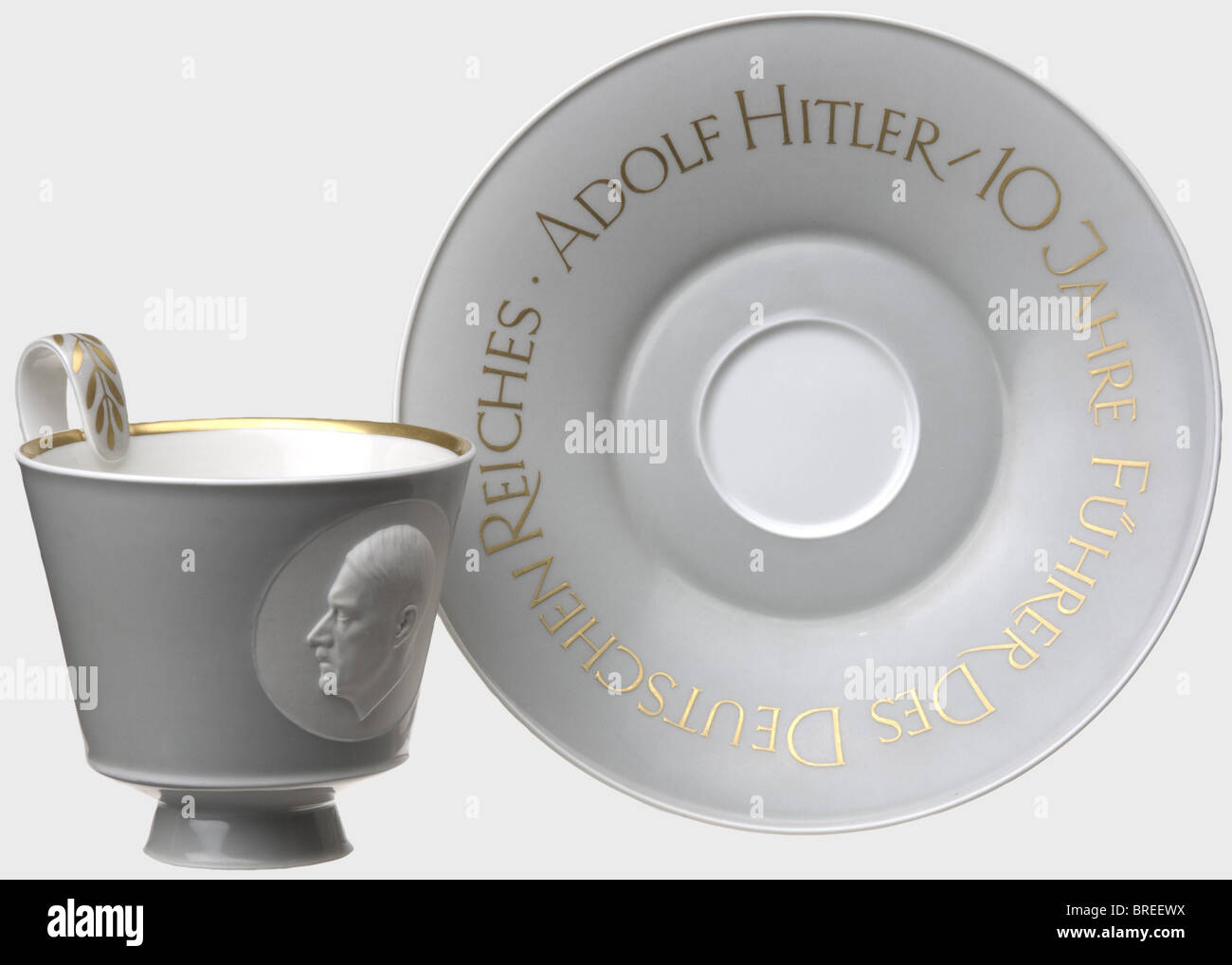 Ein KPM-Becher und eine Untertasse, Adolf Hitler/10 Jahre Führer des Deutschen Reiches Beide Außenbereiche sind aus grauglasiertem Porzellan. Der Kelch ist mit Gold verziert und trägt vorne ein unglasiertes (Keks-)Porträtmedaillon im Reliefformat. Die Untertasse zeigt die entsprechende goldene Aufschrift an. Jede hat ein blaues Zepter und eine rote orb-Markierung auf der Unterseite. Durchmesser der Untertasse ca. 19,5 cm. Cup-Höhe 9,5 cm historisch, historisch, Menschen, 1930er, 1930er, 20. Jahrhundert, NS, Nationalsozialismus, Nationalsozialismus, Drittes Reich, Deutsches Reich, Deutschland, Deutscher, Nationalsozialist, Nazi, NS-Zeit, fas, Stockfoto