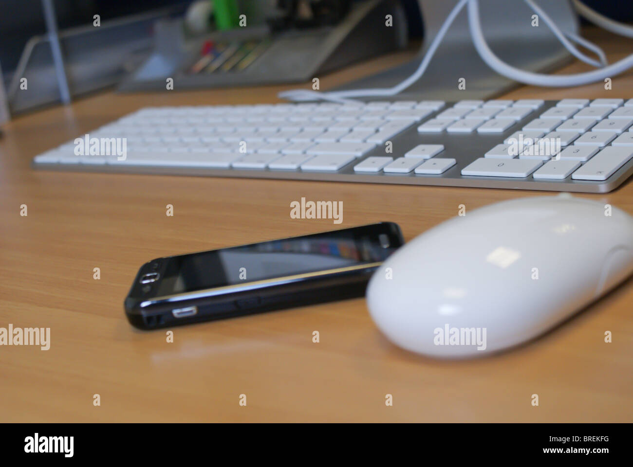 Handy auf dem Schreibtisch neben einem Apple-Maus, Tastatur und Monitor stehen. Stockfoto