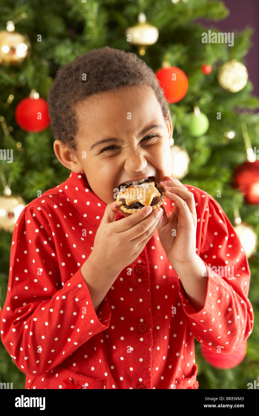 Kleiner Junge Mince Pie vor Weihnachten Baum essen Stockfoto