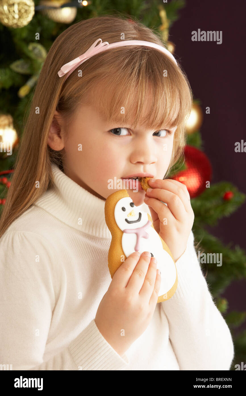 Junges Mädchen essen Cookie vor Weihnachtsbaum Stockfoto