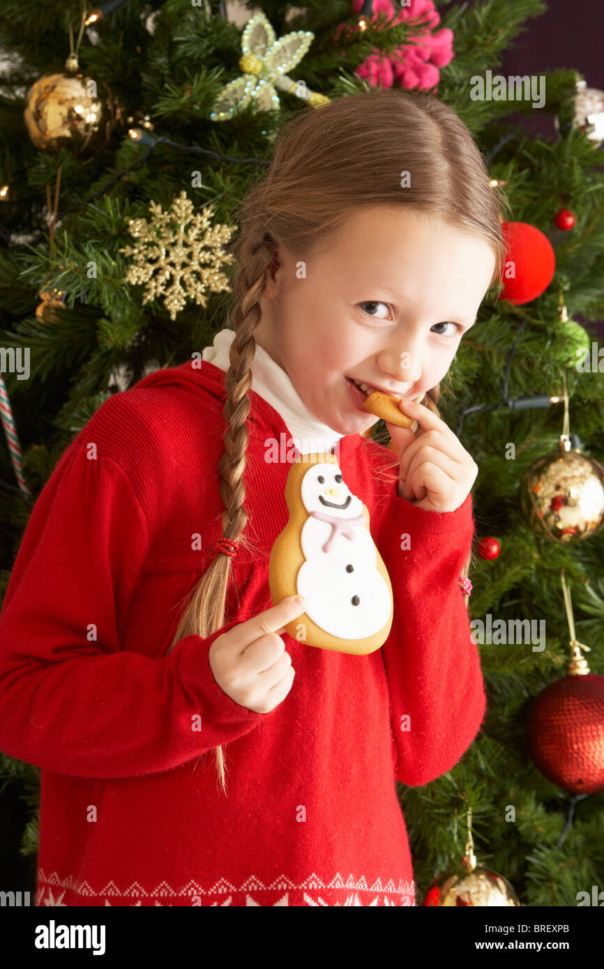 Junges Mädchen essen Cookie vor Weihnachtsbaum Stockfoto