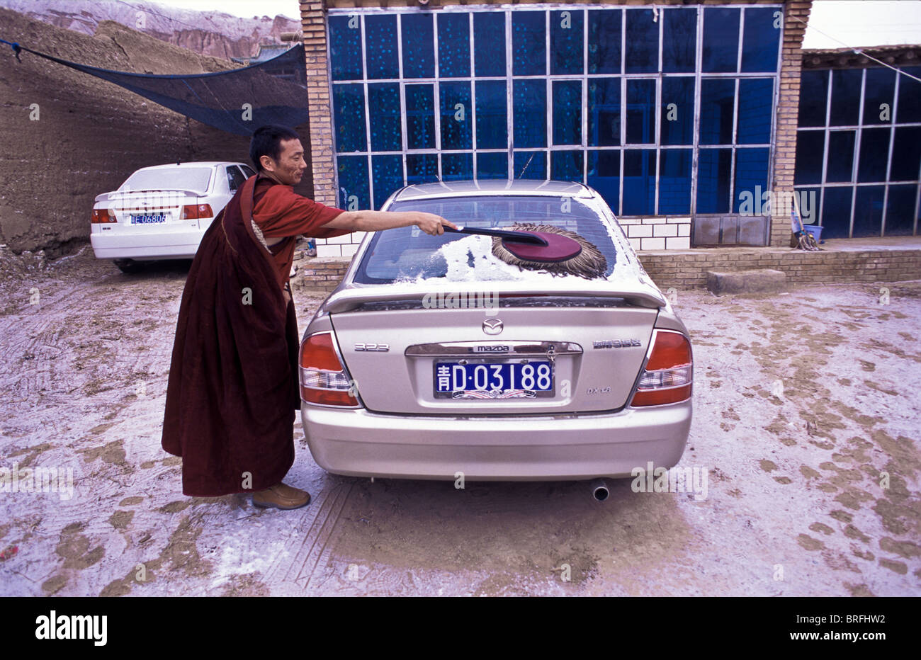 Tibetischen buddhistischen Mönch Dongyu, entfernt die Nacht Deckung der Schnee aus seinem Auto, welches Waas, die ihm von seinen Eltern vor gegeben Stockfoto