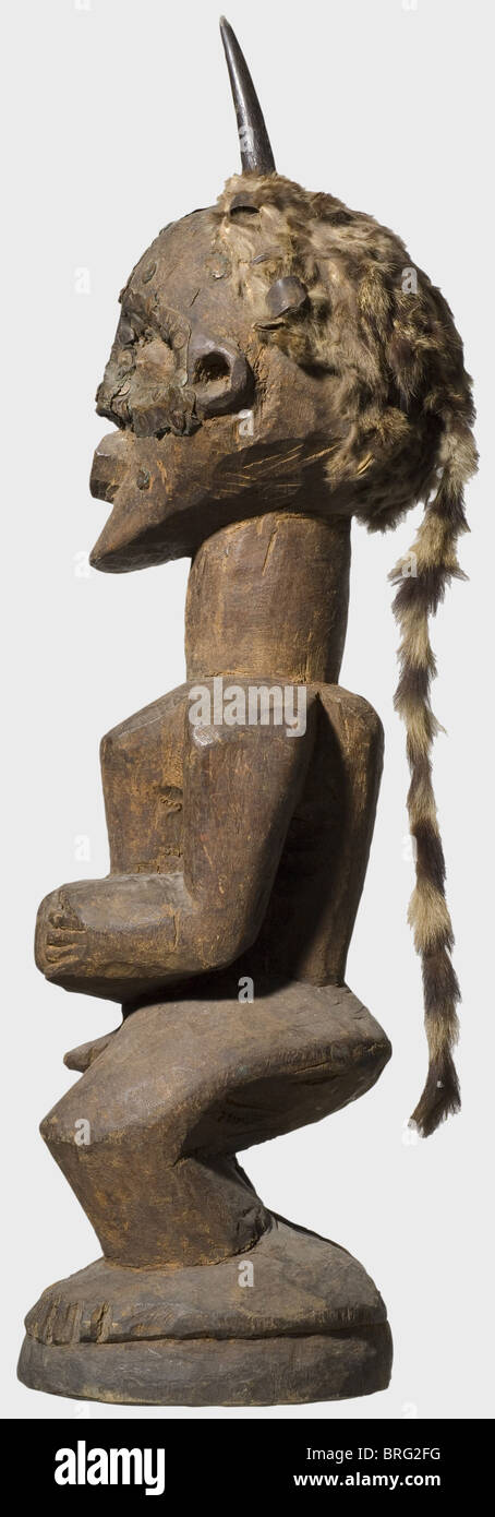 Eine Songe Nkishi Figur, Kongo, 1. Hälfte des 20. Jahrhunderts. Gehörnte Holzfigur, der Kopf mit einem Raubtier Haut Kopfschmuck. Das stilisierte Gesicht ist mit Kupferblech und Eisennägeln versehen. Der Nabel und das Stirnhorn enthalten magische Substanzen. Runder Holzsockel, die Füße sind nur grob angedeutet. Höhe 73 cm. Historisch, historisch, Menschen, bildende Kunst, Kunst, Stamm, Stämme, Stamm, Afrikaner, Afrika, ethnisch, Ethnien, Ethnologie, Ethnizität, ethnisch, exotisch, wodden, Skulptur, Skulpturen, Figur, Figuren, Objekt, Objekte, Stills, Ausschneiden, Ausschneiden, Cu, zusätzliche-Rights-Clearences-nicht verfügbar Stockfoto