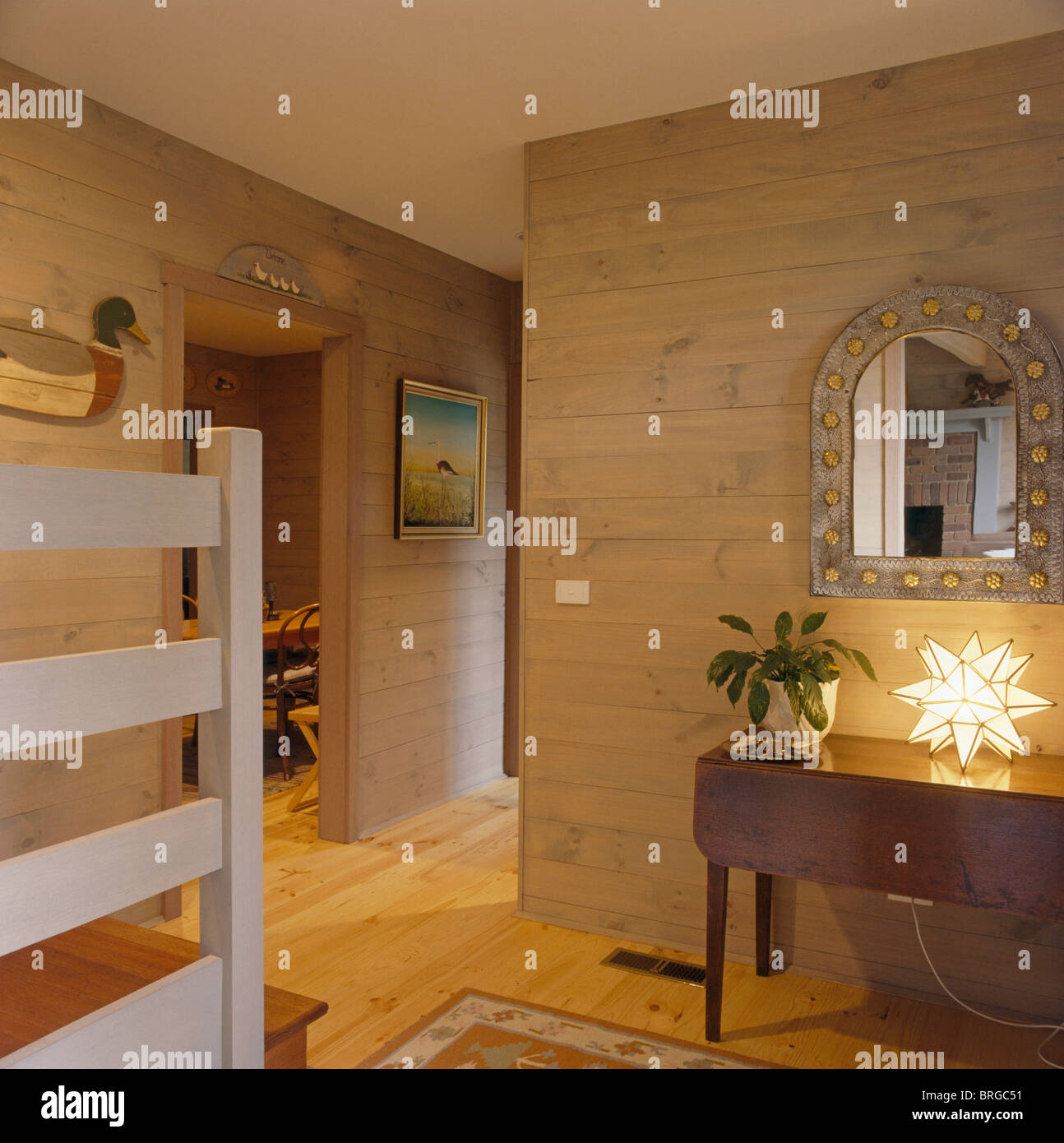 Gewölbte Metall Spiegel über Antik Konsolentisch mit sternförmigen Lampe im modernen Saal mit Holz getäfelten Wände Stockfoto