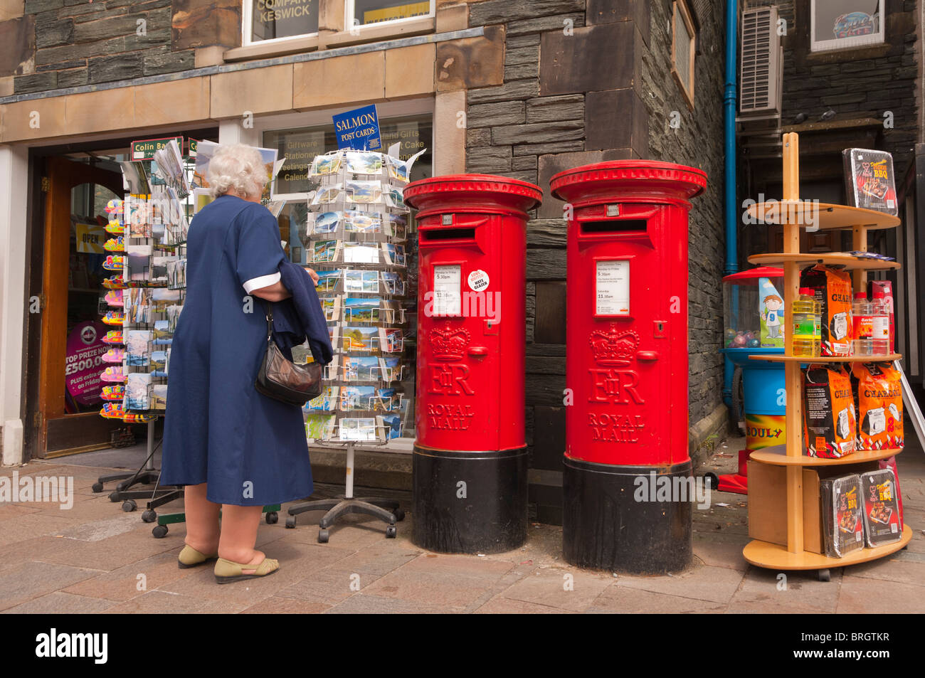Eine Frau, die Wahl einer Postkarte in The Post Office Shop speichern in Keswick, Cumbria, England, Großbritannien, Uk Stockfoto