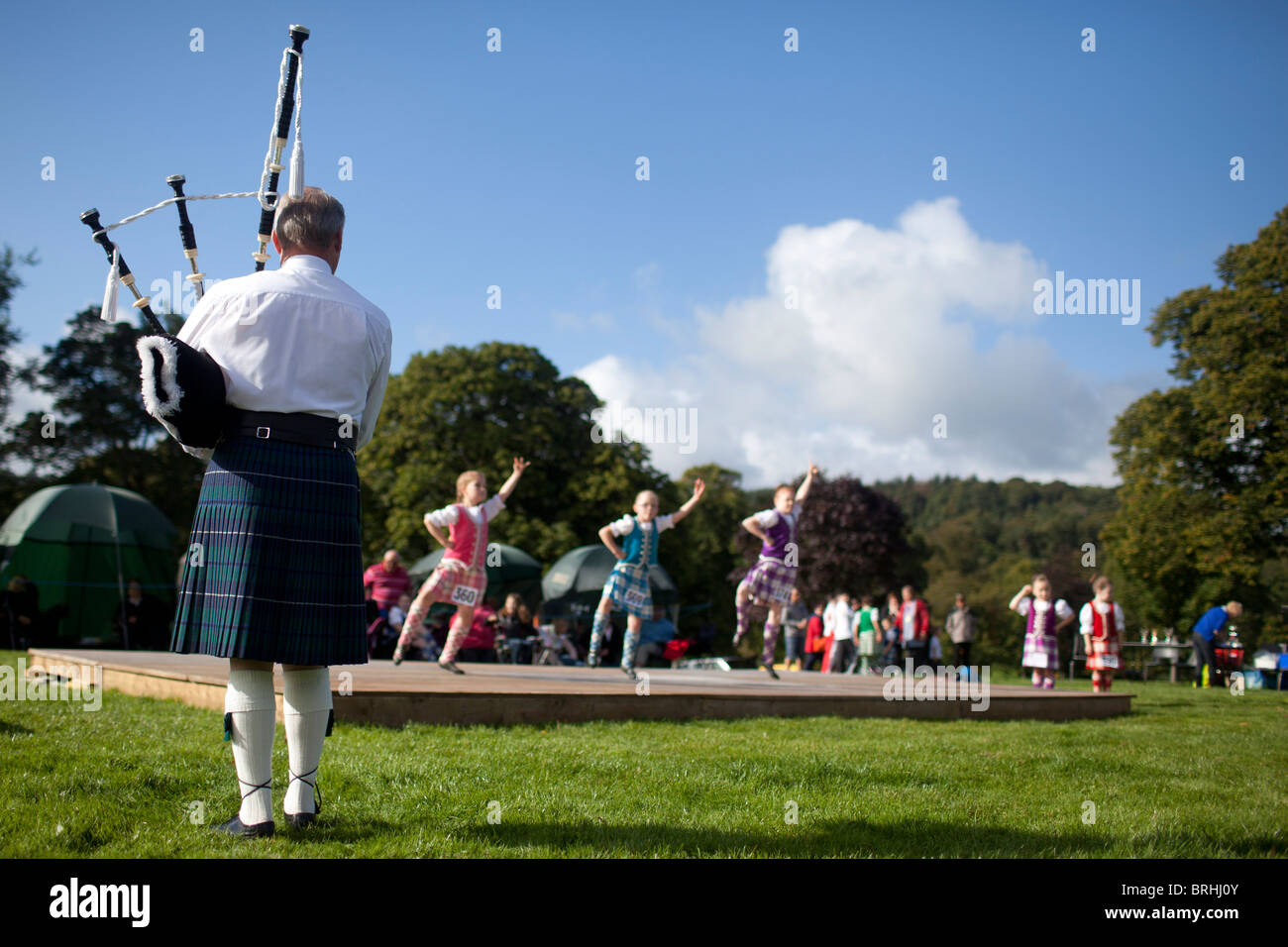 Ein Mann spielt Dudelsack für junge Highland Dancers, Peebles Highland Games, Schottland, Vereinigtes Königreich Stockfoto