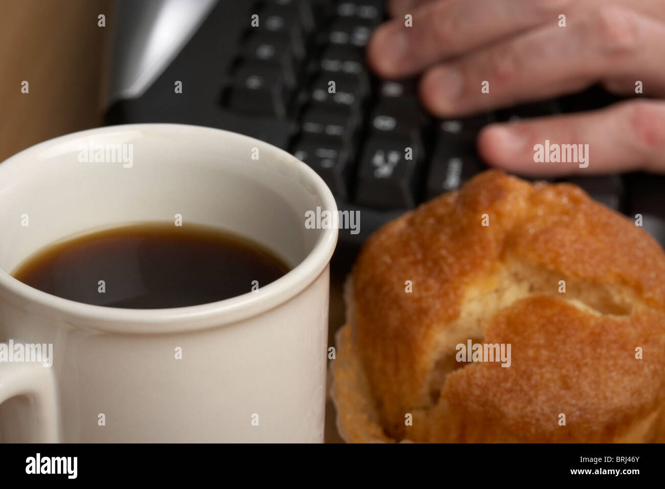 Tasse schwarzen Kaffee und ein Muffin vor einem mans Hand auf einer Computertastatur tippen Stockfoto