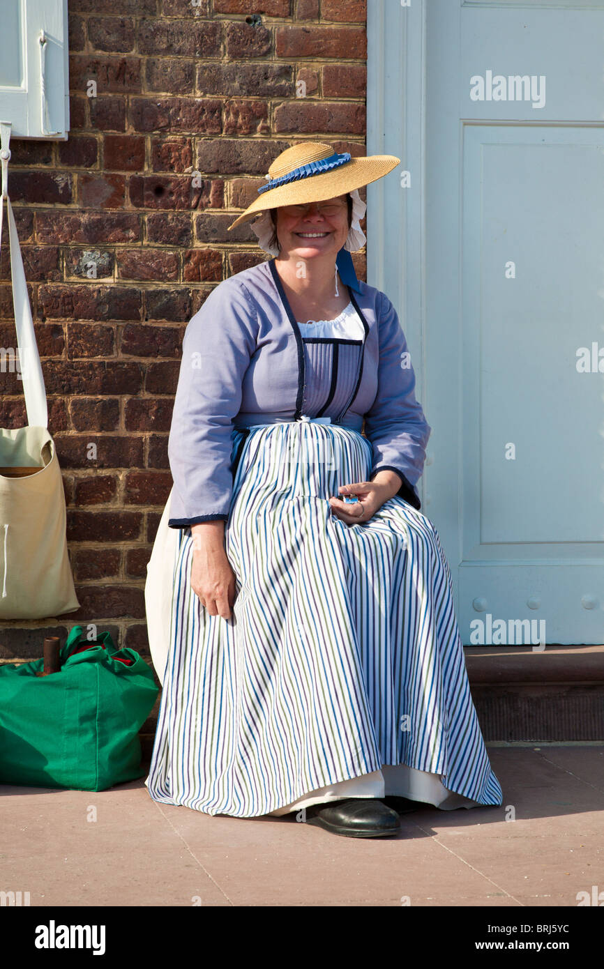 Lächelnde Frau in zeitgenössischer Kleidung gekleidet sitzt vor Haustür in Colonial Williamsburg, ein lebendiges Geschichtsmuseum in Williamsburg, VA Stockfoto